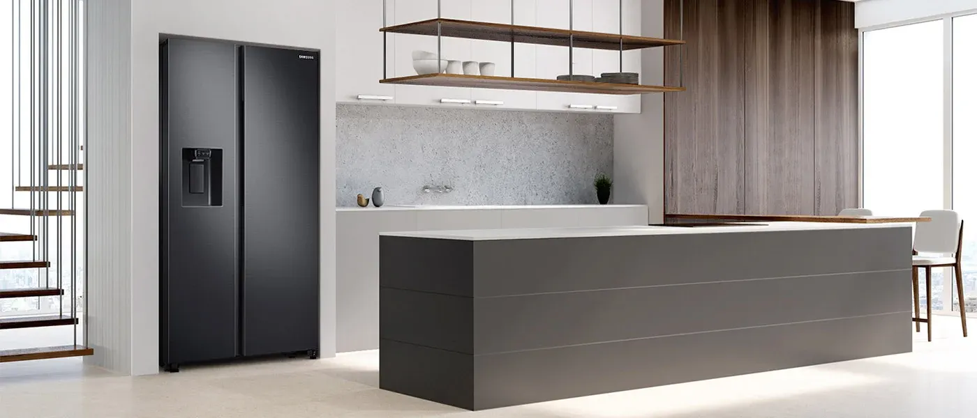 Nowoczesna kuchnia z czarną lodówką Samsung, szarą wyspą kuchenną i drewnianymi szafkami. Widoczne schody z drewnianymi stopniami.