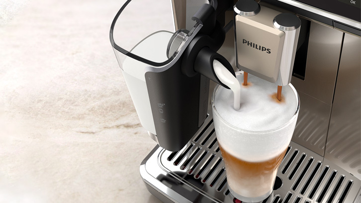 Ekspres Philips robi kawę latte do szklanki na metalowej tacce. Obok widać pojemnik na mleko.