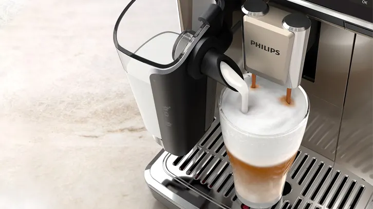 Ekspres Philips robi kawę latte do szklanki na metalowej tacce. Obok widać pojemnik na mleko.
