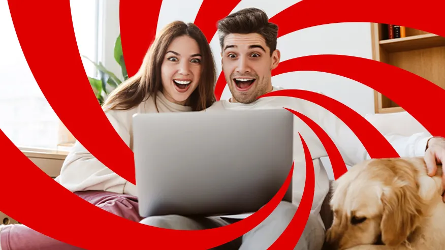 Para siedzi na kanapie z laptopem i psem, z wyrazem zaskoczenia na twarzy, na tle czerwono-białych wzorów.