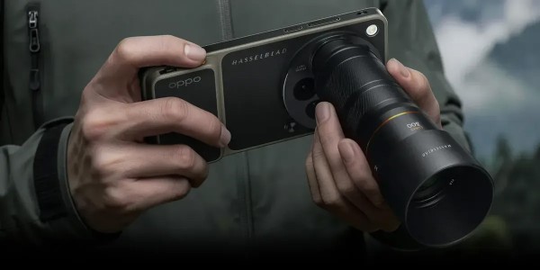 Zbliżenie: dwie dłonie trzymają smartfon OPPO z logo Hasselblad w poziomie; do aparatu zamocowany jest duży, cylindryczny obiektyw zewnętrzny; rozmyte tło plenerowe.