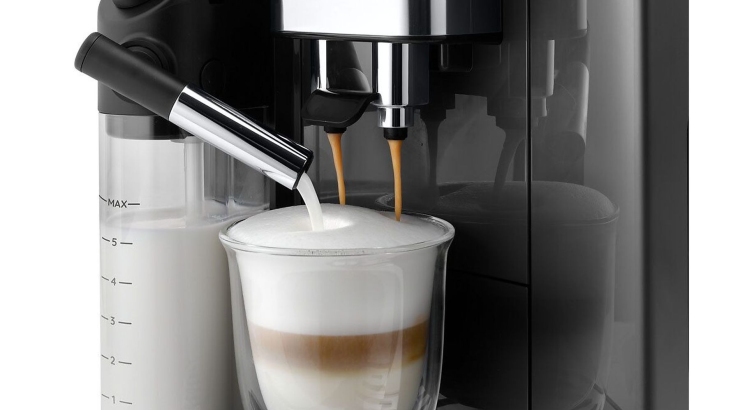 Ekspres do kawy napełnia szklankę warstwami kawy i spienionego mleka. W tle widoczny pojemnik na mleko i chromowane elementy.
