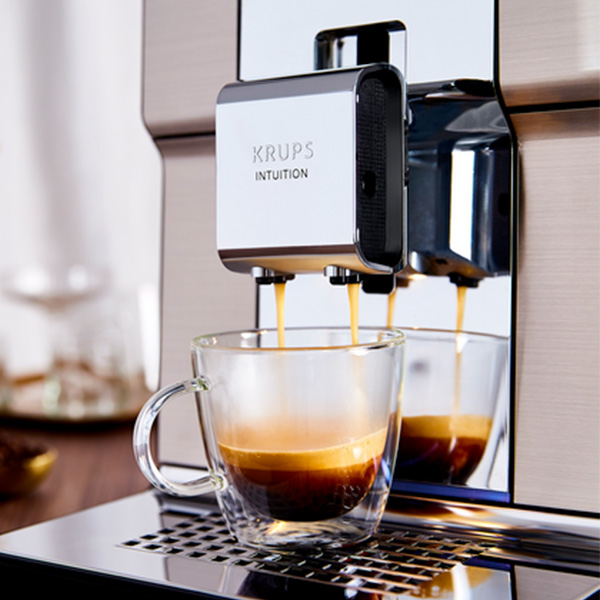 Ekspres do kawy KRUPS nalewa kawę do szklanki. Para szklanek na tacce ociekowej.