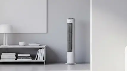 Jasne wnętrze. Widok na okno z zasłonami, regał z książkami, lampę, najlepszy wentylator kolumnowy i sofę z kwiatami. Stonowana kolorystyka.