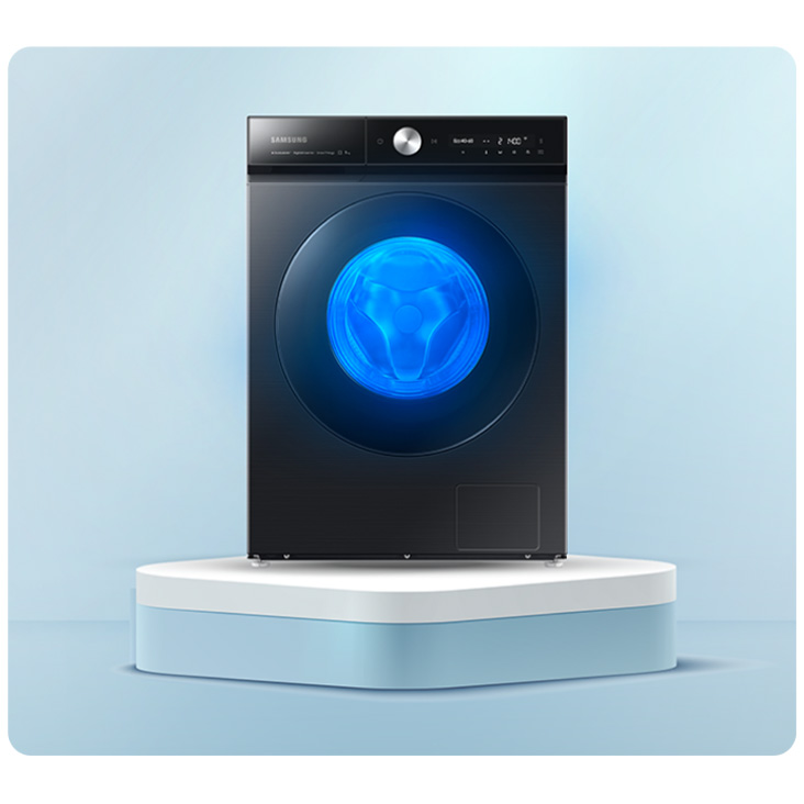 Czarna pralka na białym podeście, na tle jasnoniebieskim. Drzwi pralki okrągłe, z niebieskim światłem w środku.