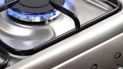 Płyta kuchenna ze stali nierdzewnej z czarnym rusztem i niebieskim płomieniem palnika.