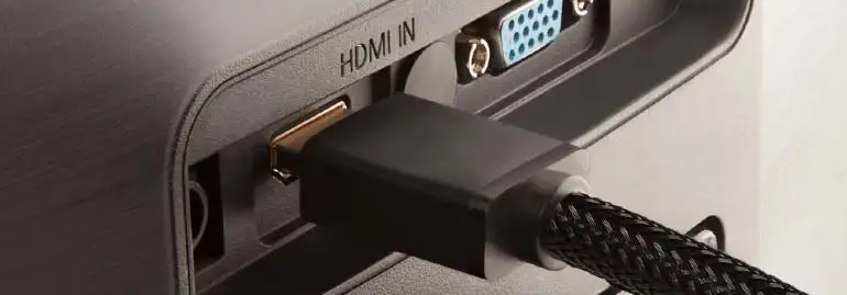 Czarny kabel HDMI wpięty do portu HDMI IN na szarym urządzeniu elektronicznym. Obok port VGA z niebieskim złączem.