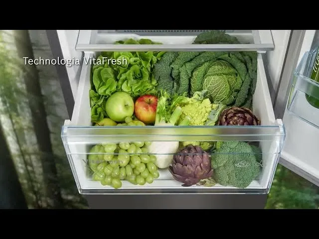 Otwarta szuflada lodówki wypełniona różnymi warzywami i owocami, w tym sałatą, kapustą, jabłkami, winogronami i karczochami.