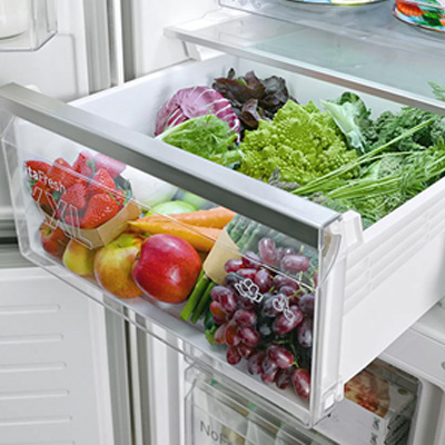 Otwarta szuflada lodówki wypełniona różnorodnymi owocami i warzywami, w tym truskawkami, jabłkami, marchewką i winogronami.