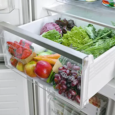 Otwarta szuflada lodówki wypełniona różnorodnymi owocami i warzywami, w tym truskawkami, jabłkami, marchewką i winogronami.