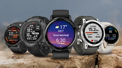 Na tle gór ustawione są zegarki Garmin na kamiennej powierzchni. Ekrany pokazują różne dane, takie jak godzina, temperatura i statystyki treningowe.
