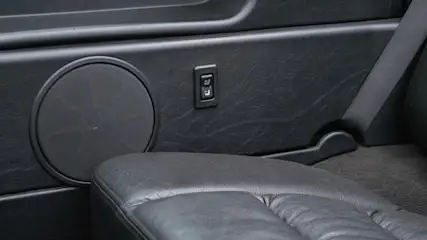 Czarny panel drzwi auta z głośnikiem, przełącznikiem i fragmentem skórzanego siedzenia z pasem.