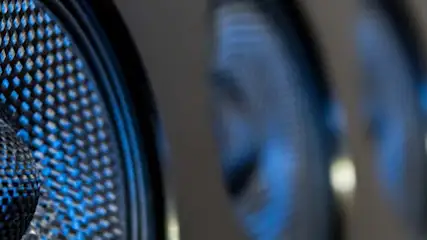 Zbliżenie na głośnik z niebieską siatką ochronną. W tle rozmyte, niebieskie kształty.