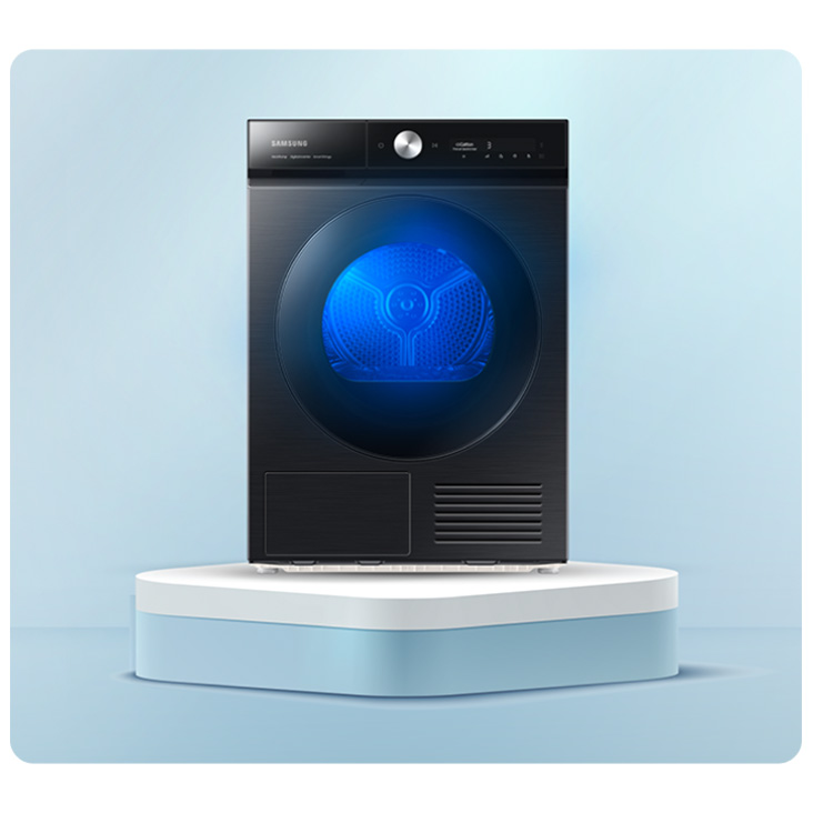 Czarna suszarka do ubrań stoi na białym podeście, na tle jasnoniebieskiego tła. Okrągłe drzwi suszarki są podświetlone na niebiesko.