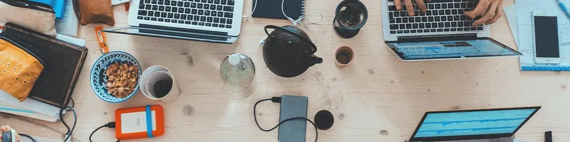 Drewniany stół pełen laptopów, powerbanków i kawy - stanowisko pracy