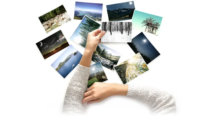 Dłonie w swetrze trzymają zdjęcia krajobrazów na białym tle. Fotografie przedstawiają lasy, góry, jeziora i nocne niebo.