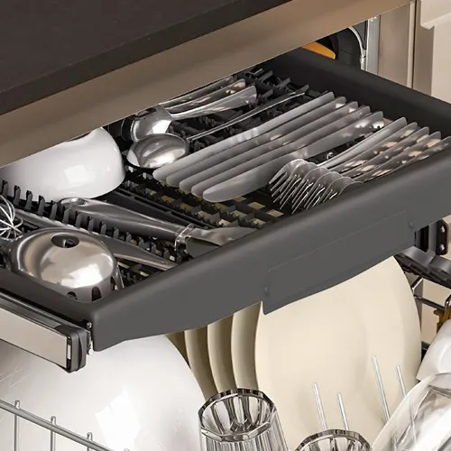 Szuflada z sztućcami w zmywarce, wypełniona srebrnymi nożami, widelcami, łyżkami i innymi przyborami kuchennymi. Poniżej białe talerze i szklanki.