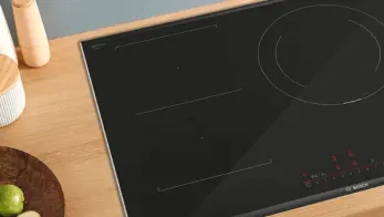 Czarna płyta indukcyjna na drewnianym blacie kuchennym. Widoczne dwa drewniane pojemniki i okrągła deska z limonką.