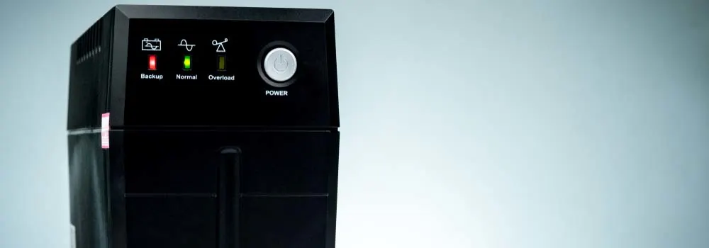 Czarna obudowa UPS z kontrolkami: backup (czerwona), normal (zielona), overload (zielona) i biały przycisk zasilania.