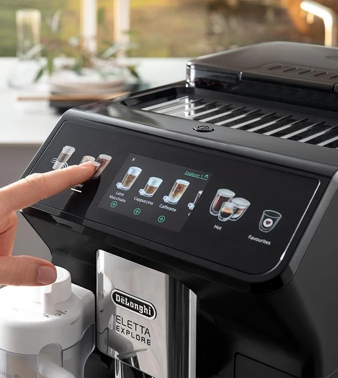 Czarny ekspres do kawy DeLonghi Eletta Explore z ekranem dotykowym, na którym palec wybiera opcję. Widoczny zbiornik na mleko.
