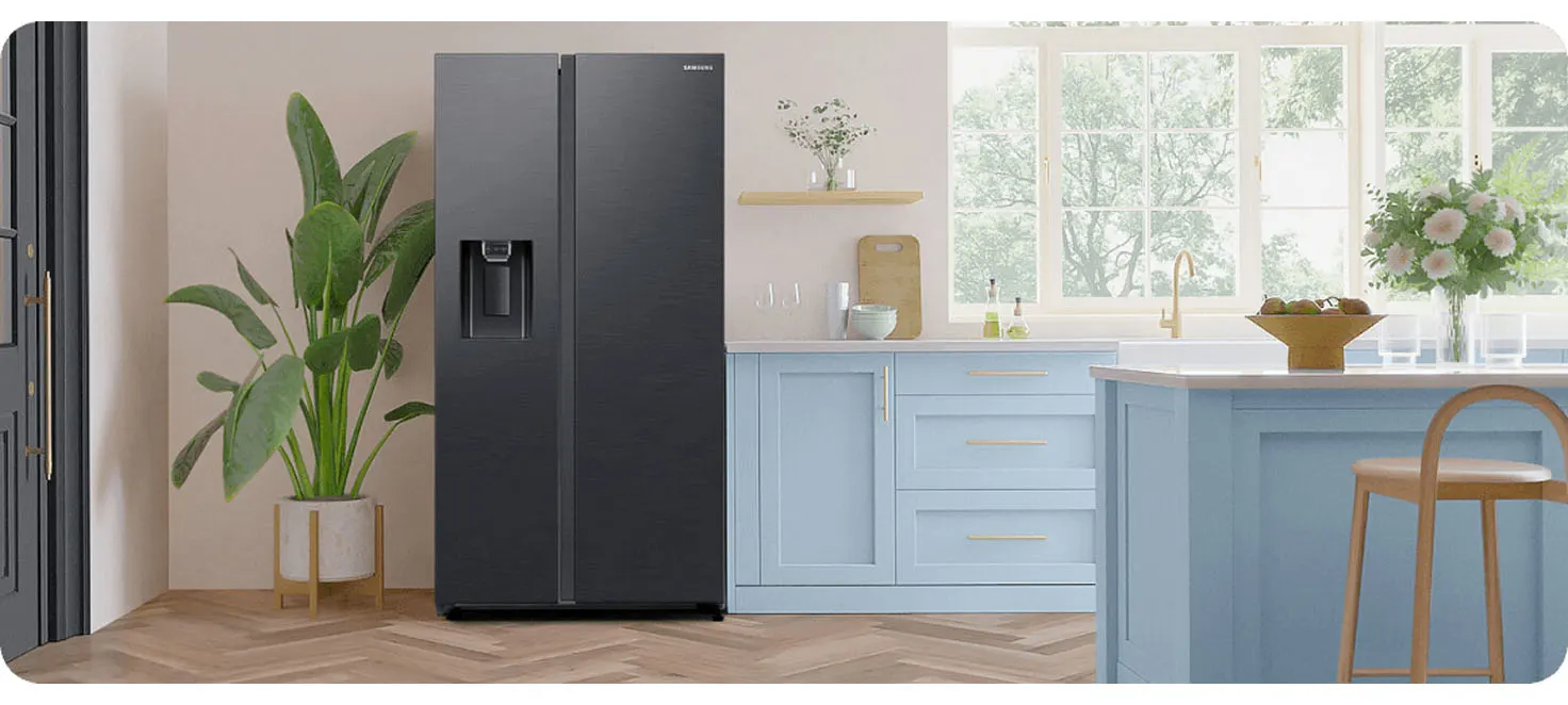 Wnętrze kuchni z czarną lodówką Samsung, rośliną w doniczce i niebieskimi szafkami. Okno w tle oświetla przestrzeń.