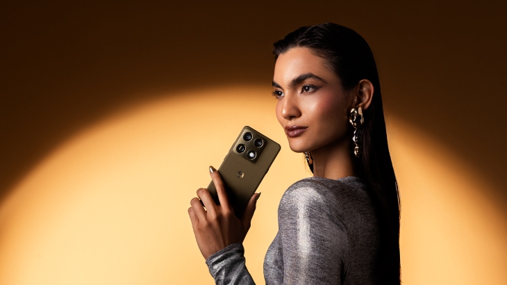 Osoba z kolczykami w uszach i długimi włosami trzyma smartfona Motorola Signature w wersji oliwkowej