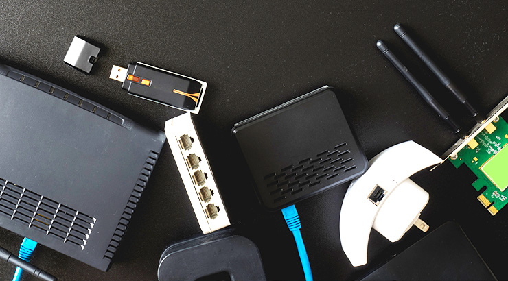 Na czarnym tle leżą router, przełącznik, karta sieciowa, adaptery i kabel Ethernet.