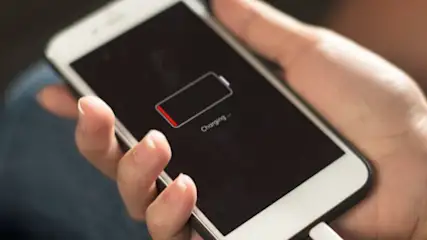 Na ekranie smartfona w dłoni widoczny jest niski poziom baterii podczas ładowania, kabel podłączony.