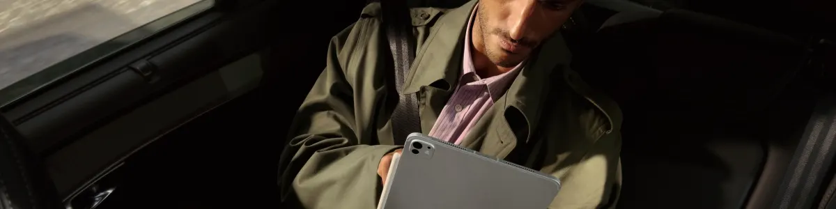 Mężczyzna w płaszczu na fotelu pasażera w samochodzie z tabletem Apple iPad Pro 2025.