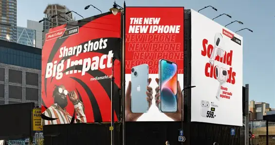 Trzy billboardy reklamowe w mieście. Jeden reklamuje telefony iPhone, drugi słuchawki, a trzeci elektronikę marki Mediamarkt.