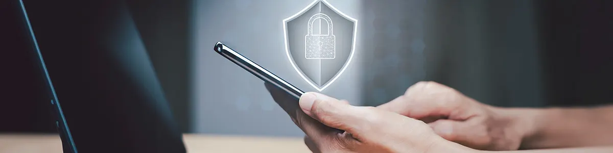 Mężczyzna z telefonem w dłoni, nad którym widoczne jest duże logo z kłódką symbolizujące ochronę przez wirusami.