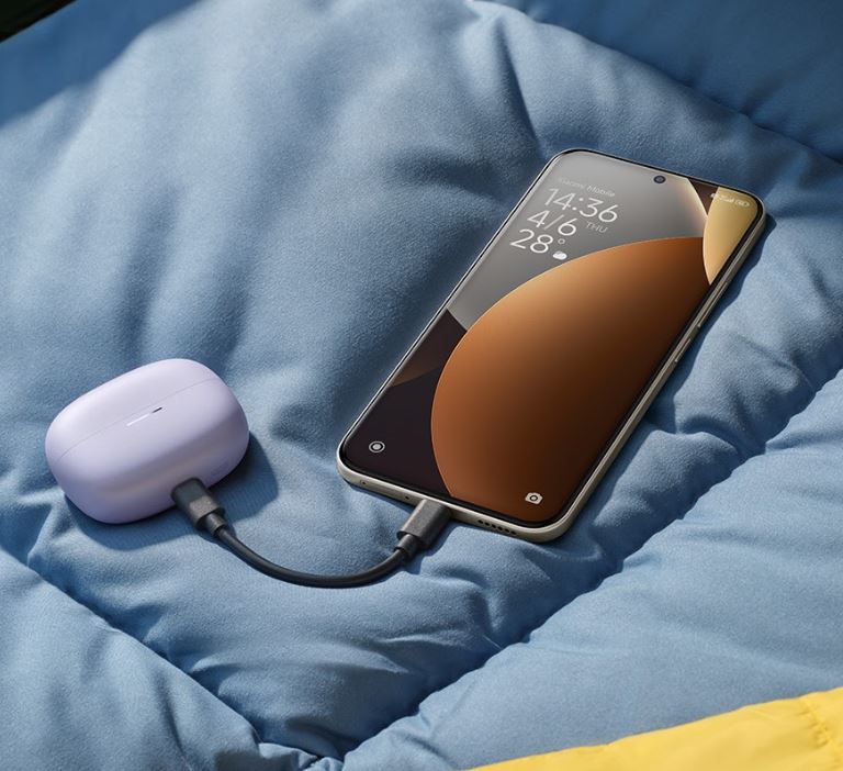 smartfon leżący na miękkim podłożu ładujący słuchawki za pomocą kabla