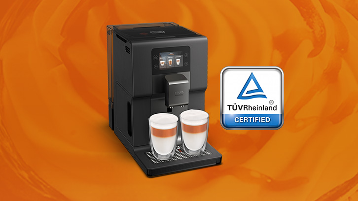 Czarny ekspres do kawy z dwoma szklankami kawy na pomarańczowym tle i logo certyfikatu.
