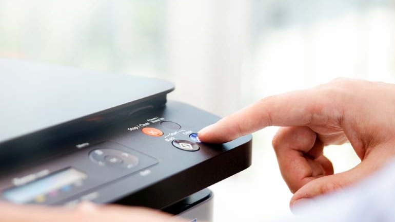 Ciemna drukarka w biurze obsługiwana przez człowieka (widoczna sama dłoń).