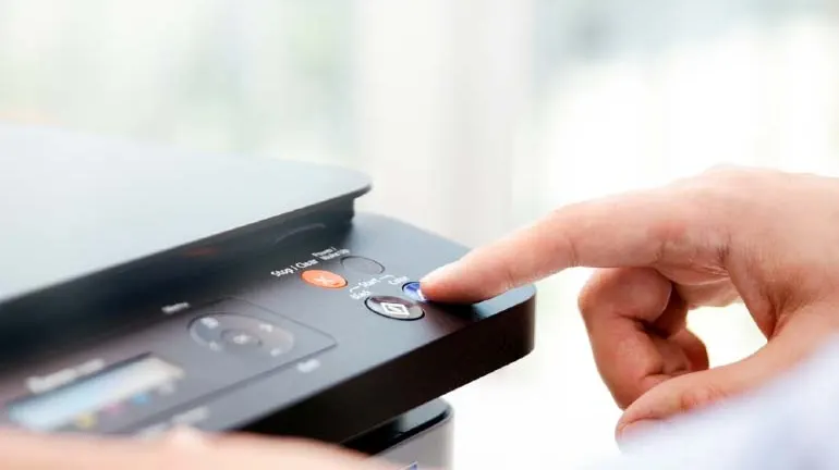 Ciemna drukarka w biurze obsługiwana przez człowieka (widoczna sama dłoń).