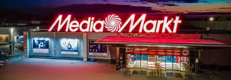 Fasada sklepu Media Markt z dużym, czerwonym neonem i szklanymi witrynami o zmierzchu.