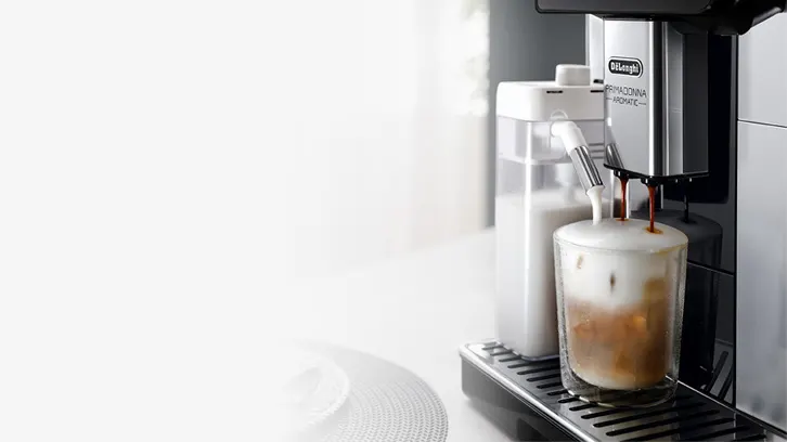 Ekspres do kawy nalewa kawę i mleko do szklanki stojącej na metalowej tacce. Obok stoi pojemnik na mleko.