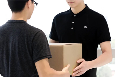 Dwie osoby wymieniają się kartonem. Obie mają na sobie czarne koszulki. Tło jest białe.