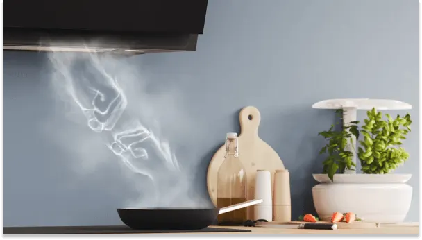 Czarny okap kuchenny nad patelnią, z której unosi się para. Obok deska, butelka, przyprawy i doniczka z ziołami na tle szarej ściany.