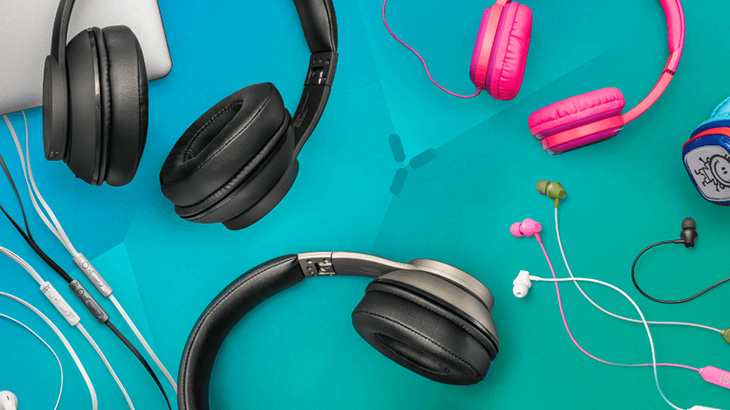 Na turkusowym tle leżą czarne, różowe i białe słuchawki nauszne i douszne z kablami.