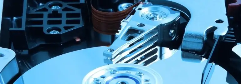 Zbliżenie na otwarty dysk twardy z widoczną głowicą i talerzami, utrzymany w chłodnej, niebieskiej tonacji.