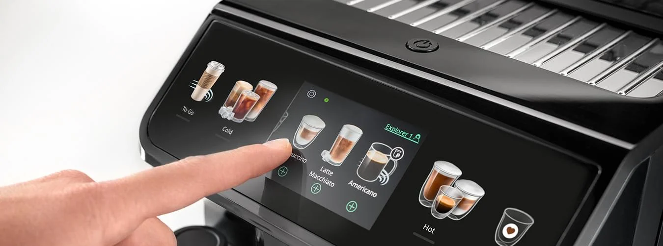 Ekspres do kawy z czarnym panelem dotykowym. Palec wybiera ikonę cappuccino. Na ekranie opcje kawy: zimna, na wynos i gorąca.