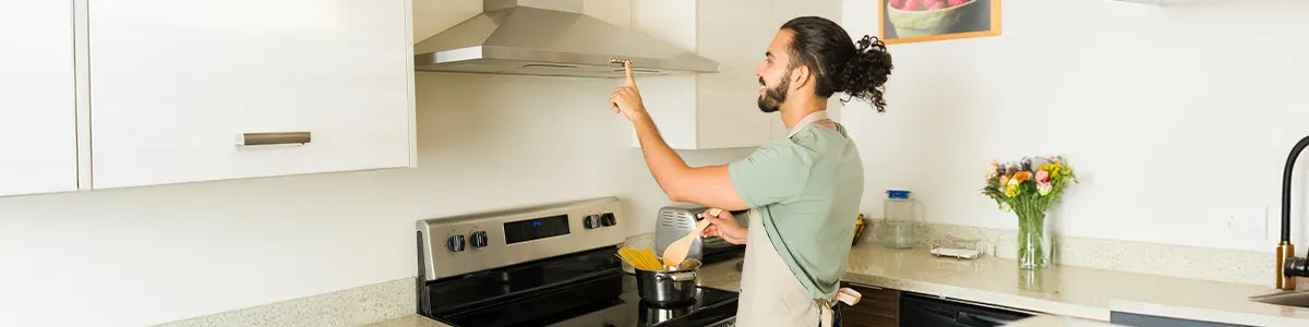 Mężczyzna naciska włącznik okapu kuchennego zawieszonego na odpowiedniej wysokości.