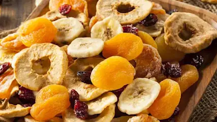 Suszone owoce, morele, banany, jabłka i żurawina na drewnianej tacy z jutowym materiałem na drewnianym stole.