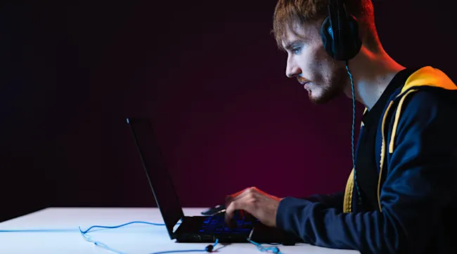 Mężczyzna w słuchawkach używa laptopa na białym stole, na ciemnym tle.