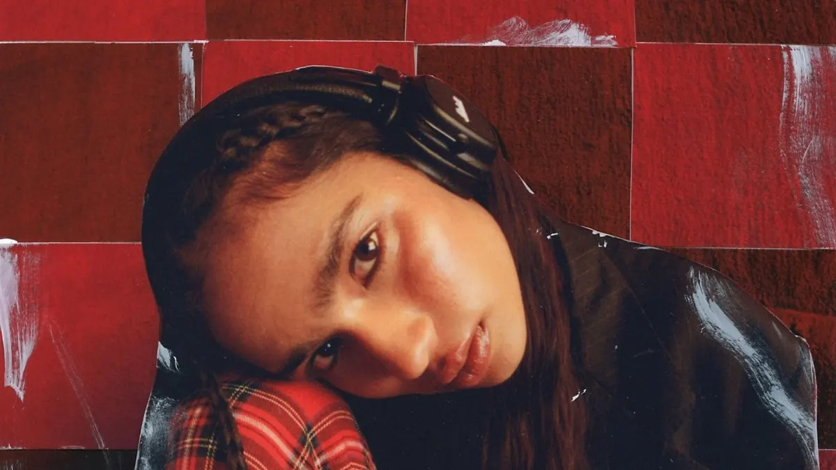 Osoba w słuchawkach opiera głowę na czerwonej koszuli w kratę. Tło to czerwono-brązowe płytki.