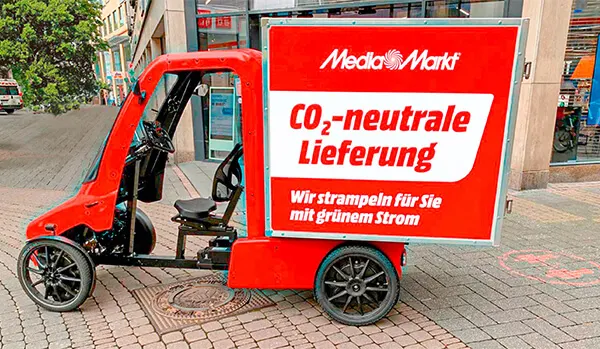 Czerwony pojazd dostawczy Media Markt z czarnymi kołami i biało-czerwonym napisem reklamowym stoi na chodniku.