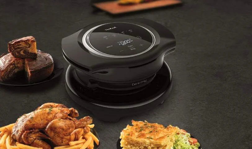 Czarny multicooker z ekranem, obok ciasto, kurczak z frytkami i zapiekanka na talerzach.