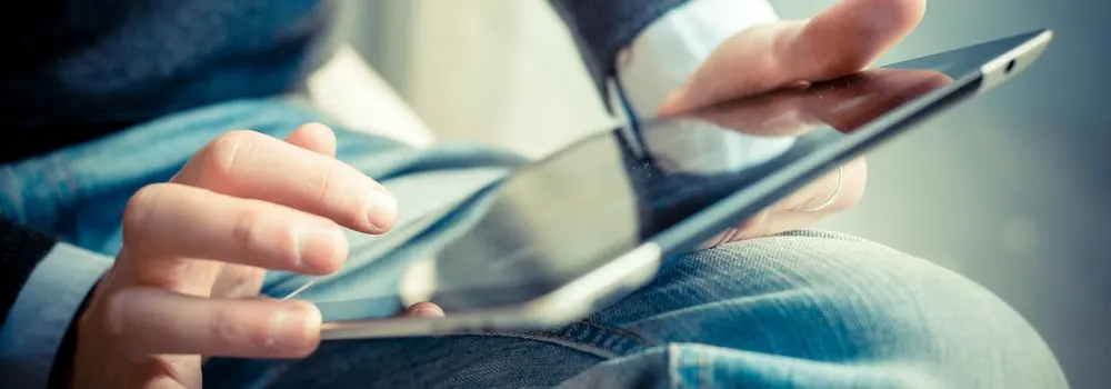 Osoba w koszuli i dżinsach trzyma tablet, dotykając ekranu palcem.