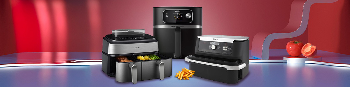 Zdjęcie przedstawia trzy frytkownice, frytki i pomidory na czerwonym tle. Frytkownice są czarne i srebrne. Frytki są żółte. Pomidory są czerwone.